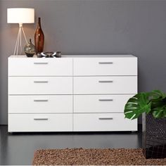 a white dresser sitting next to a lamp on top of a rug