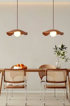 a dining table with four chairs and two hanging lights above it, in front of a white wall