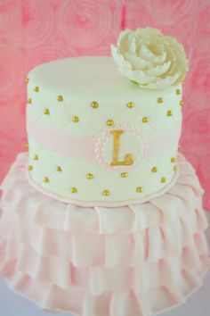 a pink and white cake with a flower on top that has the letter l on it