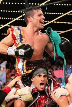 a man is holding on to another man's shoulders as he stands in the middle of a wrestling ring