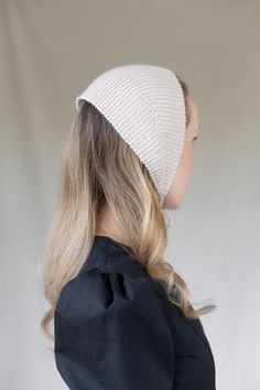 a woman with blonde hair wearing a white knitted beanie and black jacket, back view