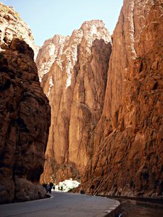 the road is surrounded by tall mountains and rocky terrain, with people walking on it