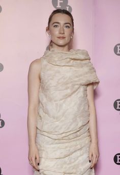 a woman standing in front of a pink wall wearing a dress with ruffles