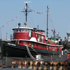 a red and white boat docked at a dock with other boats in the water behind it