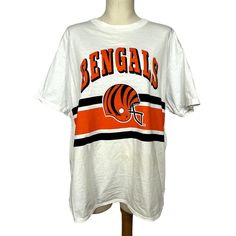 "1980s Deadstock Bengals T Shirt | Champion | XL | NWT | Vintage Super cool vintage Bengals merch! Perfect for any Bengals fan! Marked as an XL but see measurements for fit. This is a headstock Champion and is from the 80s! Measurements Bust: 50\" Waist: undefined Shoulder to Shoulder: 20.5\" Sleeve Length: 8\" Length: 28.5\" Hem: 42\" Condition: Excellent! NWT" White Throwback T-shirt For College, Retro Cotton T-shirt For Fan Gear, 90s Style Short Sleeve T-shirt For Game Day, 90s Style Cotton Top For Game Day, Vintage Graphic Print T-shirt For Game Day, 90s Style White T-shirt For College, 90s Style White T-shirt, White Cotton Throwback T-shirt, Retro Game Day T-shirt With Logo Print