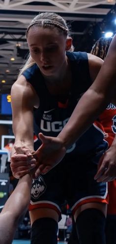 two women are playing basketball in an indoor arena, one is holding the other's leg