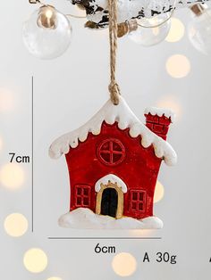 a red house ornament hanging from a tree with white lights in the background