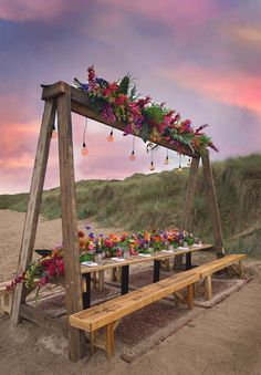 a wooden bench sitting on top of a sandy beach next to flowers and hanging lights