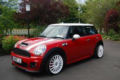 a red and white mini car parked on the side of a road in front of some trees