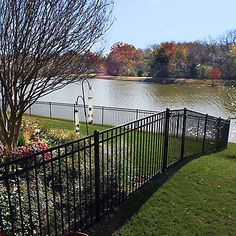 a fenced in area next to a body of water with trees and flowers around it