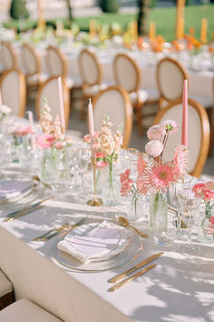 the table is set with pink and white flowers in glass vases, candles, and napkins