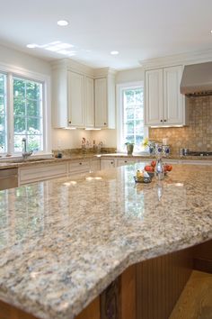 a large kitchen with marble counter tops and white cabinets, along with an island in the middle