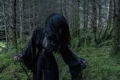 a woman dressed in black walking through the woods