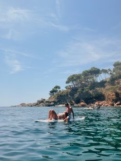 a man and woman on surfboards in the water near an island with trees behind them