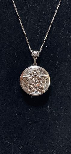 a silver locke on a black surface with an intricate design in the center and a chain around it