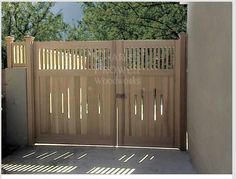 a wooden gate in the middle of a concrete area with trees and bushes behind it