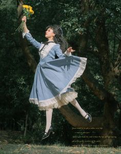 a woman in a blue dress is jumping up into the air while holding yellow flowers