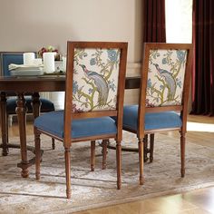 two chairs with blue upholstered back rest on a rug in front of a dining room table