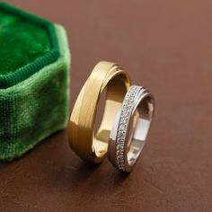 two gold and silver wedding bands next to a green velvet box on a brown surface