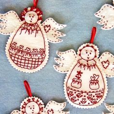 embroidered christmas ornaments with angels and snowmen hanging from red ribbon on blue fabric background