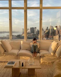 a woman sitting on a couch in front of a large window looking out at the city