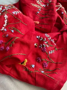 red cloth with embroidered flowers on it laying on top of a white sheet covered bed