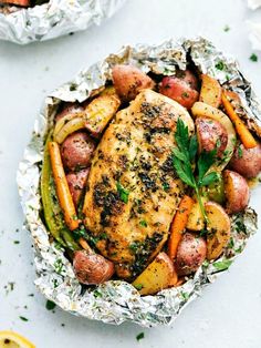 chicken, potatoes and carrots wrapped in tin foil on a table with lemon wedges