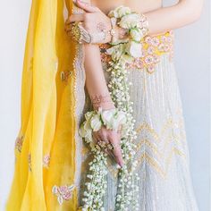 a woman in a white and yellow lehenga with flowers on her arm, wearing jewelry