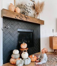 a baby sitting in front of a fireplace surrounded by pumpkins