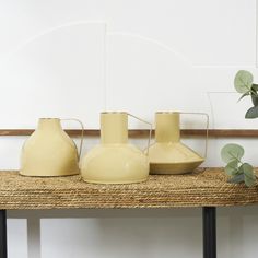 three yellow vases sitting on top of a shelf next to a potted plant