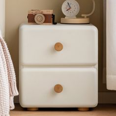 a white dresser with two drawers and a clock on top