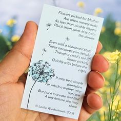 a person holding up a card with a dandelion on it in front of some yellow flowers