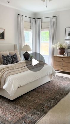 a large white bed sitting in a bedroom next to a window with curtains on it