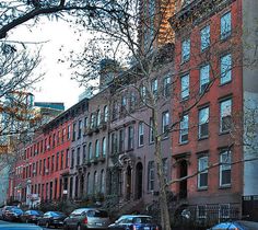 several cars parked on the side of a street next to tall brick buildings and trees