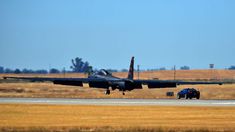 a fighter jet taking off from an airport runway with a car in the foreground