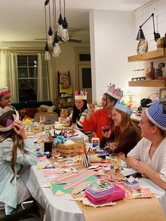 a group of people sitting around a table with hats on top of them and cake in front of them