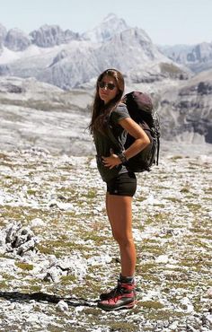 a woman standing on top of a snow covered slope with a backpack in her hand