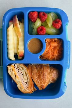 a blue plastic lunch box filled with fruit and vegtables on top of it