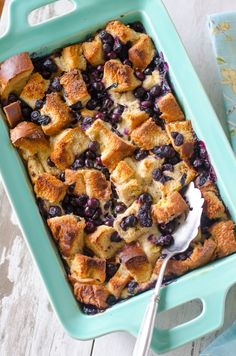 blueberry cobbler with ice cream on top in a green baking dish next to a spoon