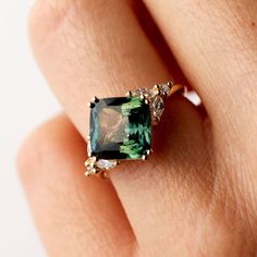 a woman's hand with a green ring on top of her finger and an emerald colored stone in the middle