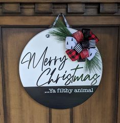 merry christmas ya filthy animal sign hanging on the side of a door with pine branches