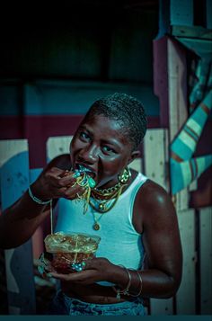 a woman eating food from a bowl in front of her face and wearing necklaces