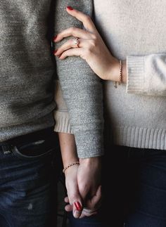 two people holding hands while standing next to each other in front of a building with red nail polish on their fingers