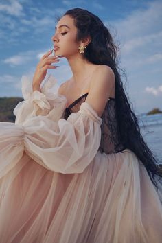 a woman in a long dress sitting on the beach with her hands to her face