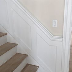 a cat sitting on top of some stairs next to a wall with a light switch