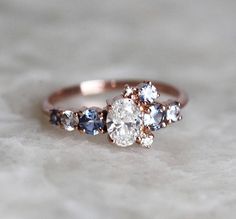 an engagement ring with three different colored stones on it's side, sitting on a marble surface