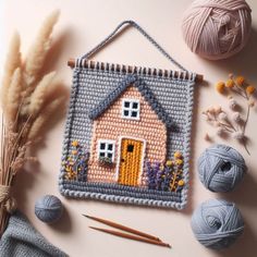 a cross stitch house is on the table next to yarn, needles and balls of yarn