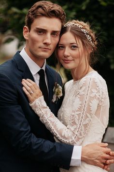 a man in a suit and tie hugging a woman wearing a white lace wedding dress