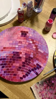 a pink mosaic plate sitting on top of a wooden table next to paint and brushes