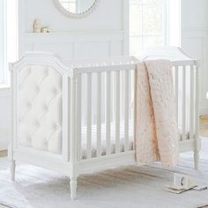 a white baby crib with a pink blanket on the floor and a mirror above it